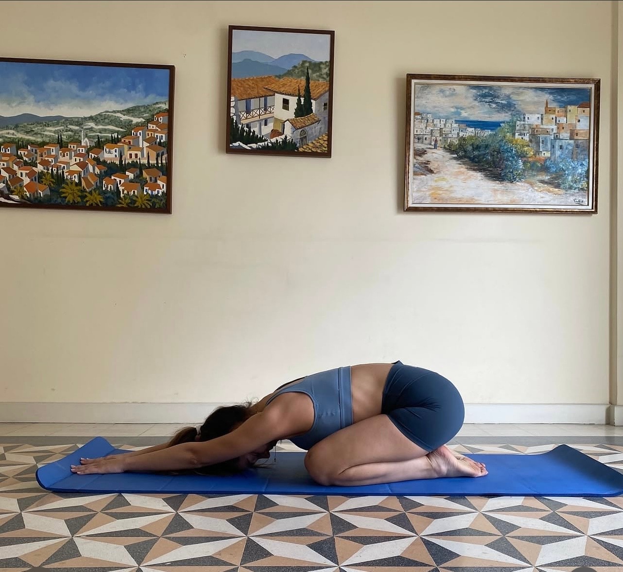 Woman performing a child’s-pose movement exercise on a blue mat