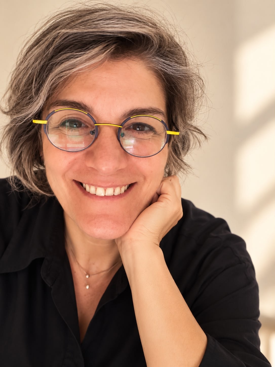 Doress Naffaa smiling in glasses and a black shirt, resting her cheek on her hand